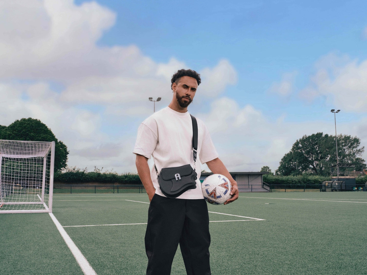 Man holding a soccer ball on a sports field with a clear sky