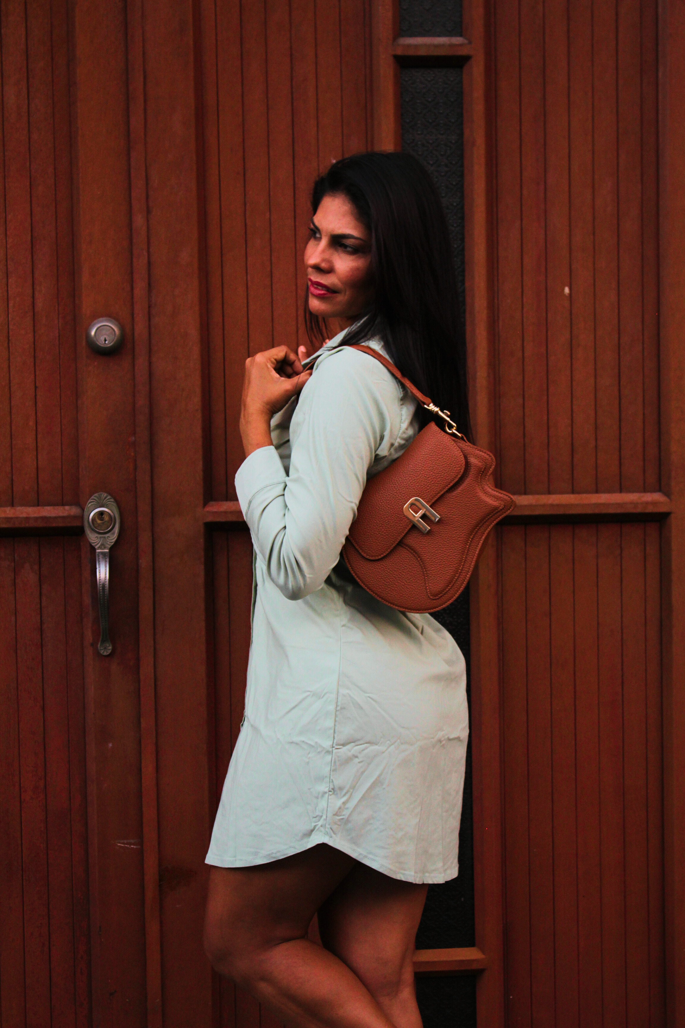Woman holding a brown leather bag against a wooden door