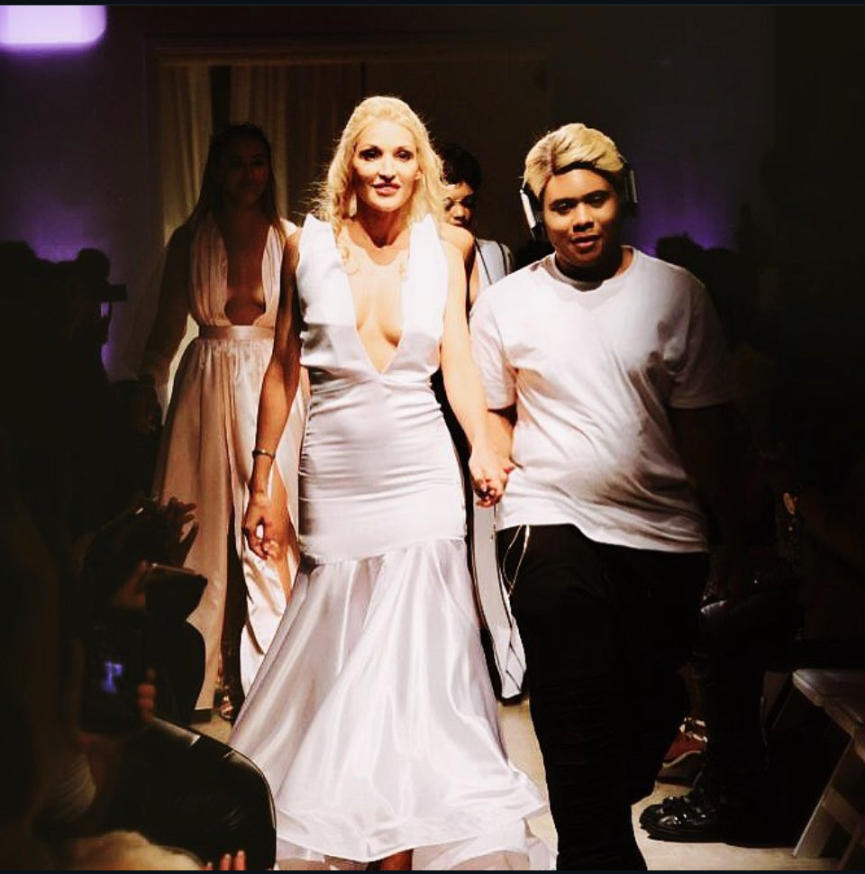 Woman in a white dress walking with a man in a white shirt at an event.