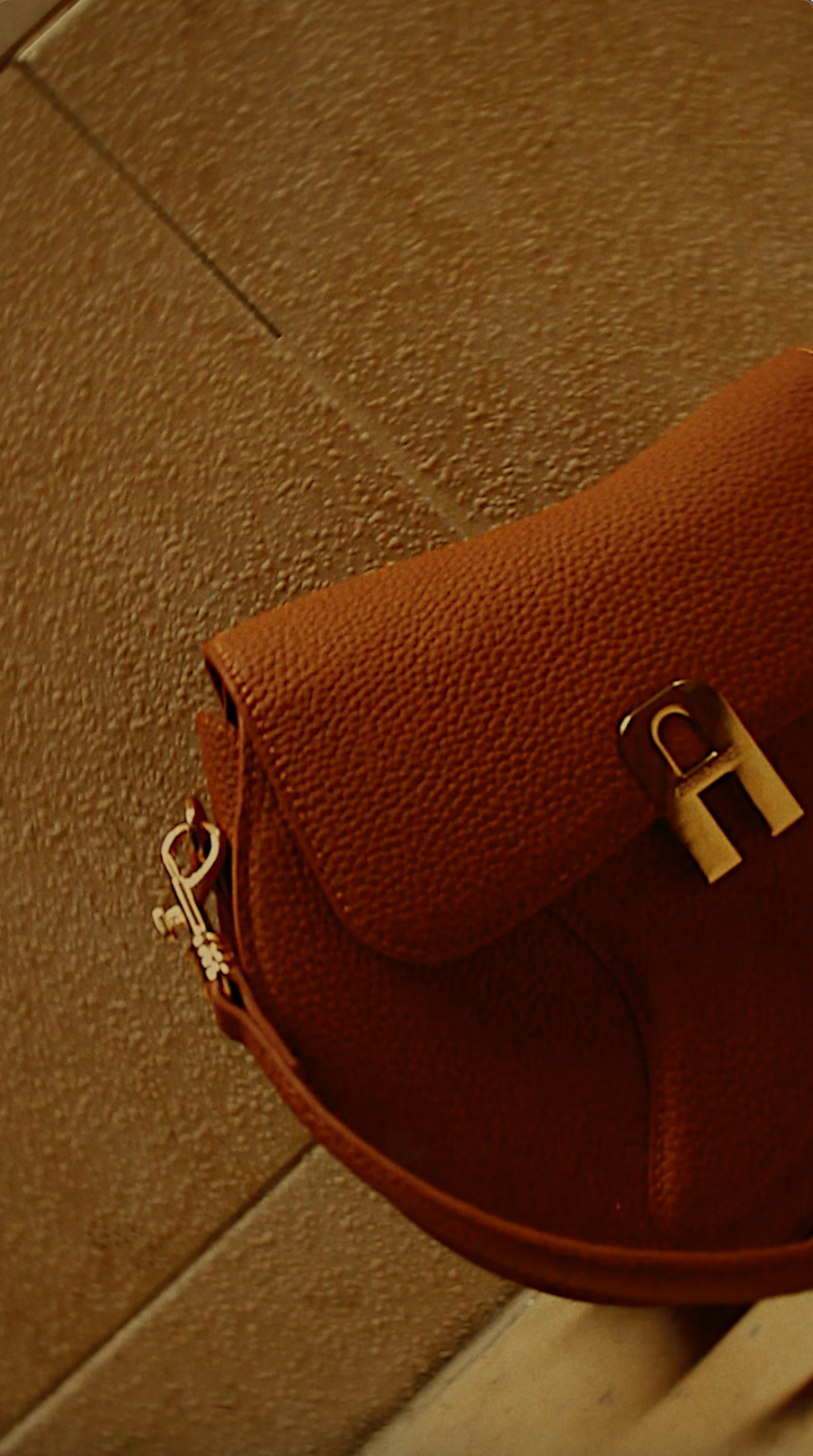 Brown leather handbag with a gold clasp on a brown textured surface